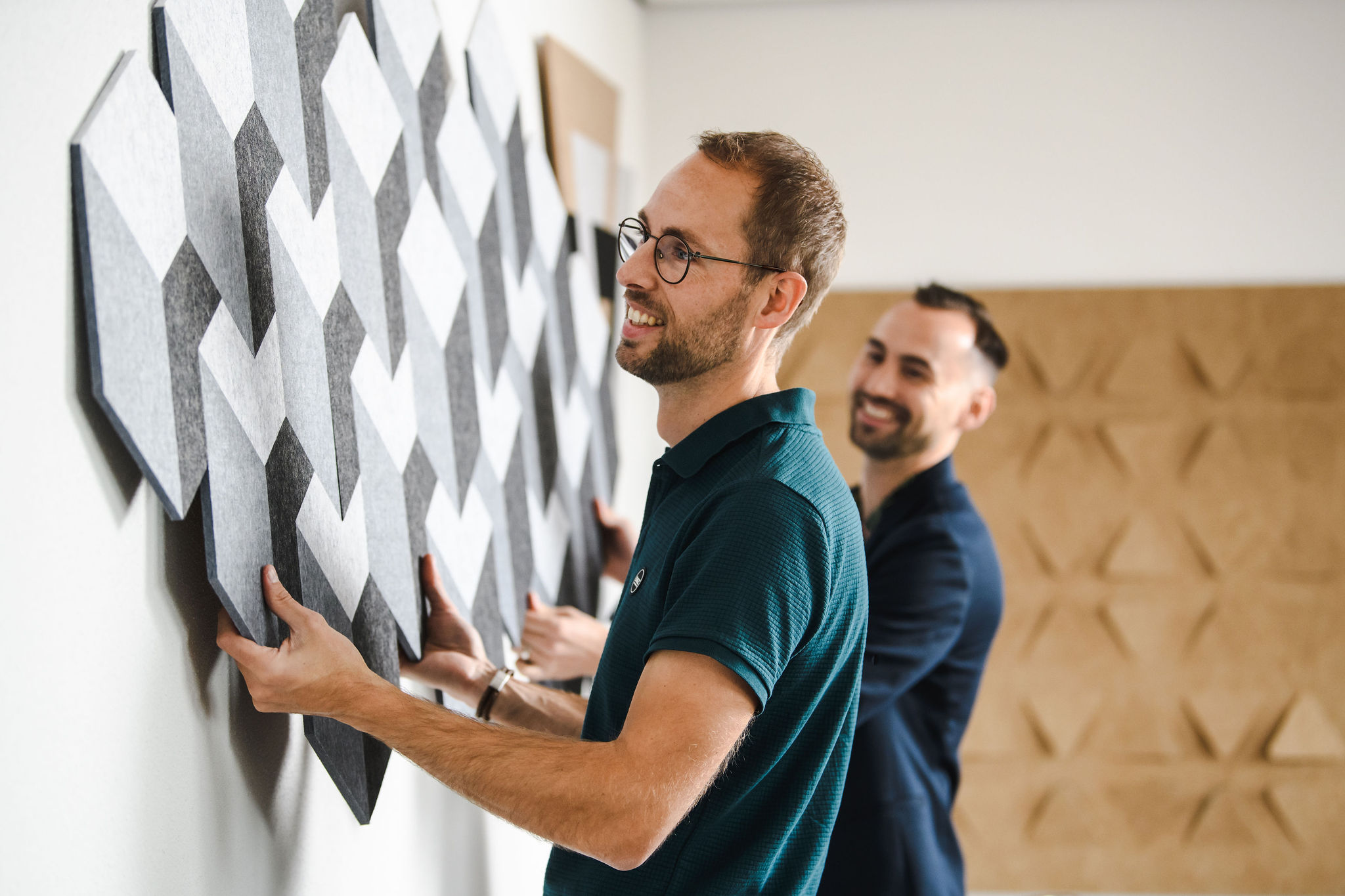 Two Viltr team members installing a wall of grey felt panels
